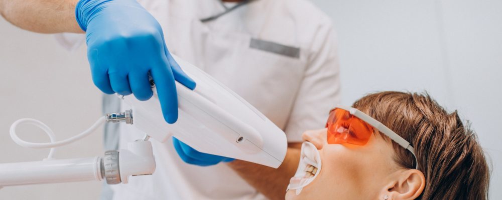 Woman whitening teeth at dentistry with special equipment